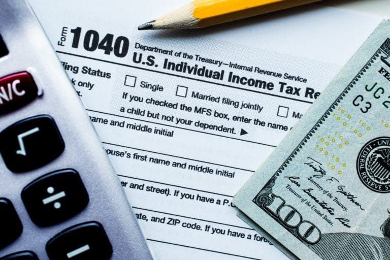 A calculator, a 1040 tax form, a $100 bill, and a pencil